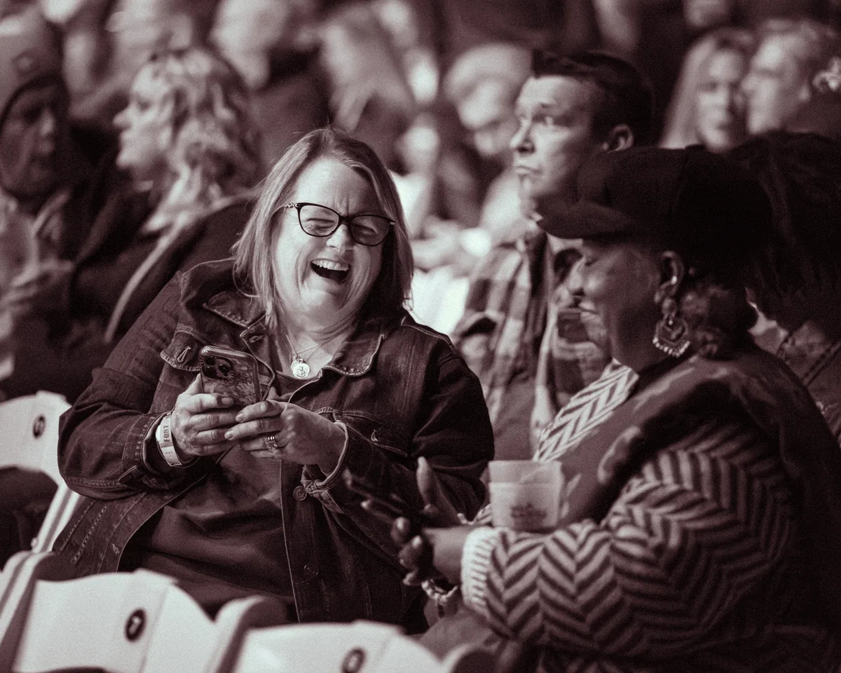 Woman laughing enthusiastically while holding phone at Fort Mose Jazz Festival in St. Augustine, Florida